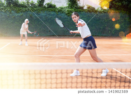 Middle aged and senior women plays tennis on open court with opponent. Middle aged and senior women plays tennis on open court with opponent. 141902389