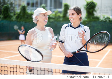 Elderly and young woman chatting on tennis court Elderly and young woman chatting on tennis court 141902391