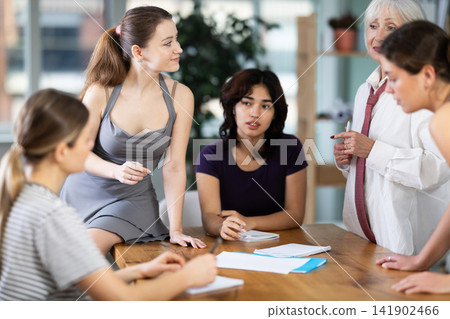 Interested office female workers sitting at table with papers and discussing ideas during business meeting in office Interested office female workers sitting at table with papers and discussing ideas during business meeting in office 141902466
