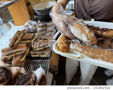 Customer Picking Fresh Baked Baguette and Salt Bread onto Tray at Bakery 141902502