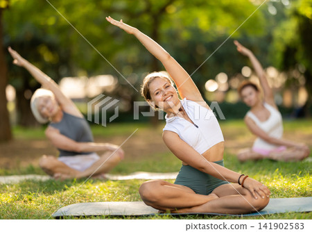 Girl stretching in lotus position at group yoga class outdoors Girl stretching in lotus position at group yoga class outdoors 141902583