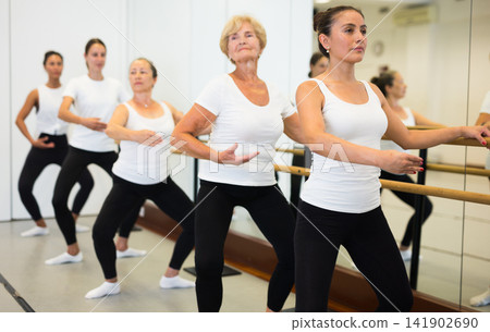 Young Latin American woman does demi plie near the ballet barre, standing in a ballet stance Young Latin American woman does demi plie near the ballet barre, standing in a ballet stance 141902690