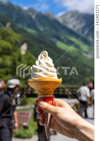 Kamikochi: A soft-serve ice cream cone held in the hand with the Hotaka mountain range in the background - Summer sightseeing. Kamikochi: A soft-serve ice cream cone held in the hand with the Hotaka mountain range in the background - Summer sightseeing. 141903571