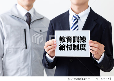 一位身穿西裝的年輕商人,手持一塊白板,上面寫著關於教育和培訓福利計畫的內容。 一位身穿西裝的年輕商人,手持一塊白板,上面寫著關於教育和培訓福利計畫的內容。 141904431