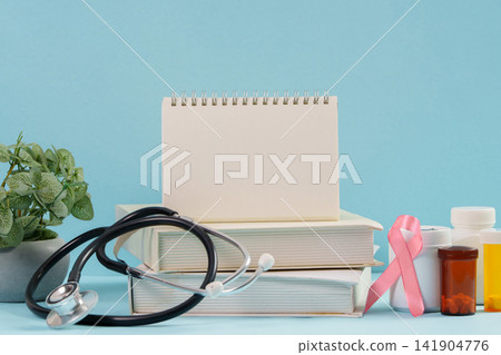 Breast cancer awareness concept with stethoscope notepad books and pink ribbon on blue background Breast cancer awareness concept with stethoscope notepad books and pink ribbon on blue background 141904776