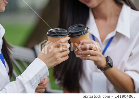 Close up of colleagues clinking coffee cups together during break outdoors Close up of colleagues clinking coffee cups together during break outdoors 141904863