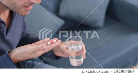 Cropped view of man holding pills and glass of water for medication routine Cropped view of man holding pills and glass of water for medication routine 141904864
