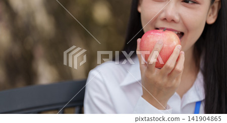 Asian woman biting into fresh red apple outdoors for healthy nutrition and dental care Asian woman biting into fresh red apple outdoors for healthy nutrition and dental care 141904865
