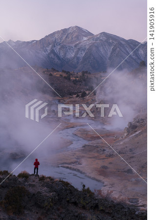 Solitary hiker admires steam over hot spring valley near sierra nevada mountain range feeling peaceful wonder during serene dawn Solitary hiker admires steam over hot spring valley near sierra nevada mountain range feeling peaceful wonder during serene dawn 141905916