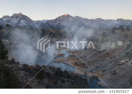 Steaming hot spring landscape in sierra nevada mountain valley evokes serene wonder under clear twilight sky with distant snow peak Steaming hot spring landscape in sierra nevada mountain valley evokes serene wonder under clear twilight sky with distant snow peak 141905917