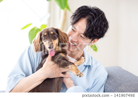 與狗共度的家庭生活:一位男士和他的狗在沙發上放鬆。 與狗共度的家庭生活:一位男士和他的狗在沙發上放鬆。 141907498