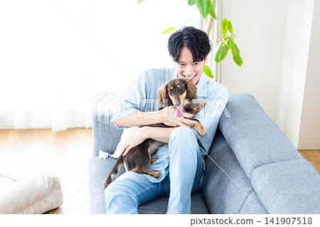 與狗共度的家庭生活:一位男士和他的狗在沙發上放鬆。 與狗共度的家庭生活:一位男士和他的狗在沙發上放鬆。 141907518