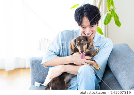 與狗共度的家庭生活:一位男士和他的狗在沙發上放鬆。 與狗共度的家庭生活:一位男士和他的狗在沙發上放鬆。 141907519