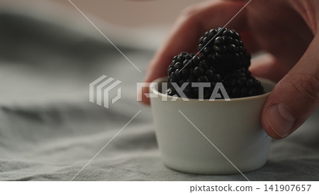 man hand put fresh ripe blackberry in a white small bowl man hand put fresh ripe blackberry in a white small bowl 141907657