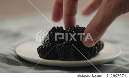 man hand put fresh ripe blackberry on a white saucer man hand put fresh ripe blackberry on a white saucer 141907674