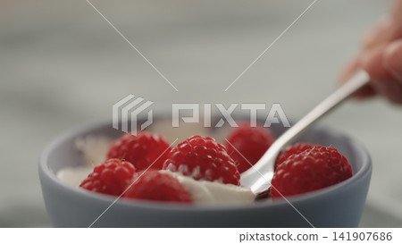 taking a spoon of raspberries with yogurt from a bowl taking a spoon of raspberries with yogurt from a bowl 141907686