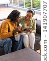 African American couple sitting on balcony, man in mustard sweater holding card, woman using tablet 141907707