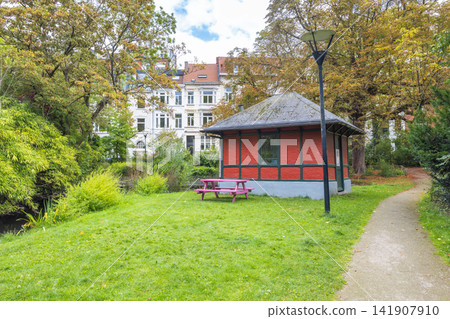 Ghent town in Belgium, Europe. Charming Red Pavilion and Picnic Table in a Lush Green Park Setting with Historic Buildings and Autumn Trees 141907910