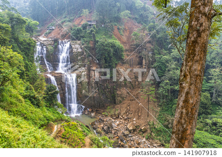 Ramboda Waterfall near Nuwara Eliya town in Sri Lanka. Misty Tropical Waterfall Cascading Down Rocky Slopes Amidst Lush Green Rainforest During Overcast Day Ramboda Waterfall near Nuwara Eliya town in Sri Lanka. Misty Tropical Waterfall Cascading Down Rocky Slopes Amidst Lush Green Rainforest During Overcast Day 141907918