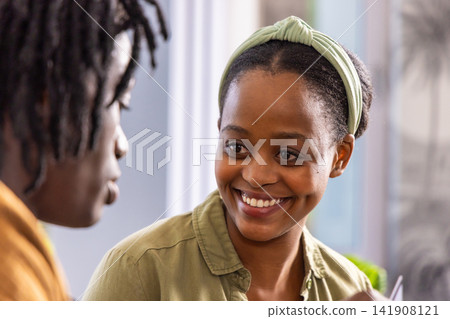 African American adult friends smiling and talking at home, woman wearing olive shirt and headband 141908121