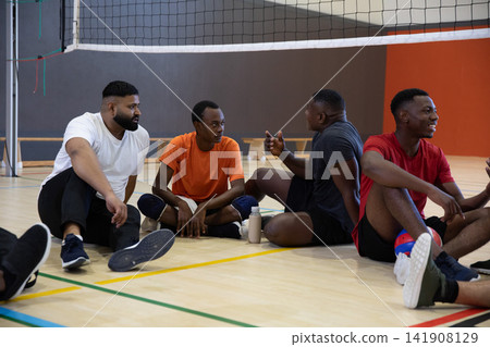 African American men sitting and chatting on hardwood volleyball court near net, wearing knee pads African American men sitting and chatting on hardwood volleyball court near net, wearing knee pads 141908129