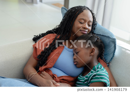 African American mother and youth daughter resting on beige sofa at home, sleeping, bangles showing 141908179