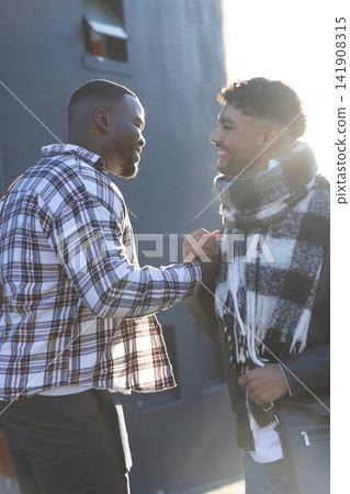 Diverse male friends greeting near dark wall wearing plaid shirt scarf carrying messenger bag 141908315