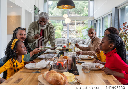Multigenerational African American family gathering at wooden dining table at home, passing platter Multigenerational African American family gathering at wooden dining table at home, passing platter 141908330