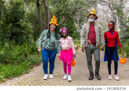 African American family walking path with kids wearing pumpkin hats with orange buckets dog behind African American family walking path with kids wearing pumpkin hats with orange buckets dog behind 141908334