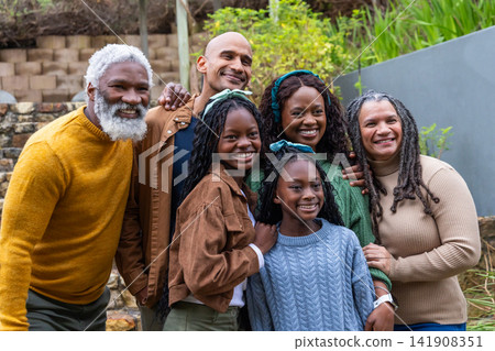 Diverse multi-generational family standing on stone steps by retaining wall, wearing knit sweaters 141908351