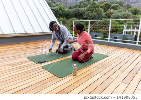 African American couple kneeling, stretching in sportswear on rooftop with mats, phone and bottle African American couple kneeling, stretching in sportswear on rooftop with mats, phone and bottle 141908355