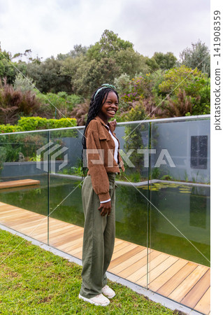 African American female standing, smiling beside glass rail at garden pond with lilies and headband African American female standing, smiling beside glass rail at garden pond with lilies and headband 141908359