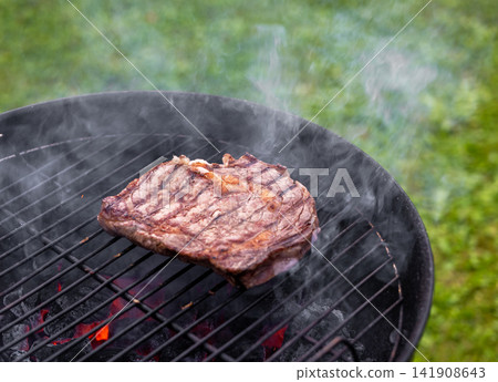 Juicy Beef Steak Grilling on Charcoal Barbecue in Garden 141908643