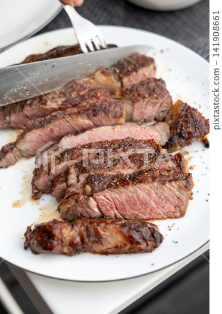Slicing Freshly Grilled Beef Steak on Plate on Garden Terrace Table Slicing Freshly Grilled Beef Steak on Plate on Garden Terrace Table 141908661