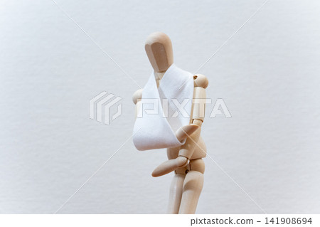A drawing mannequin with a triangular bandage on its arm. 141908694