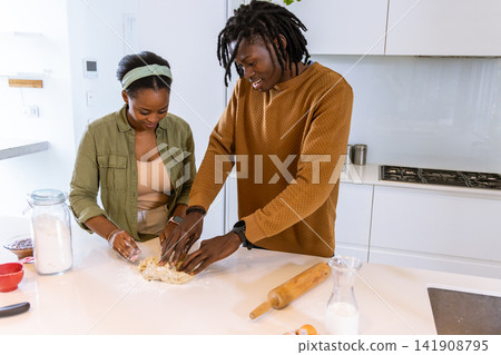 African American couple kneading dough, smiling on white counter in modern kitchen with flour jar 141908795