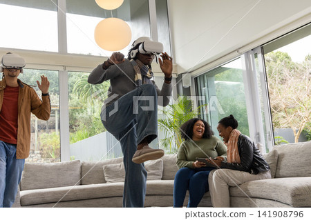 Diverse friends using white VR headsets and interacting with tablet in modern living room Diverse friends using white VR headsets and interacting with tablet in modern living room 141908796