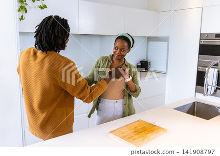 African American couple standing at white island in kitchen holding hands near chest, cutting board 141908797