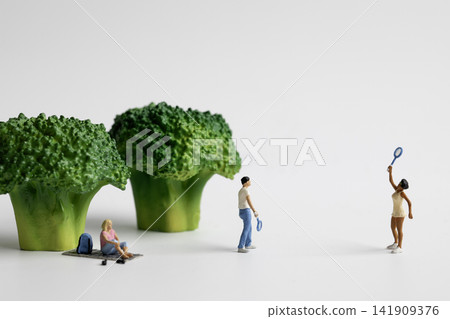 A miniature woman sitting under green broccoli and a couple playing badminton 141909376