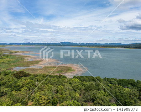 Drone aerial view of a large freshwater lake bordered by lush forest and distant mountains beneath expansive blue skies, showcasing natural landscape and tranquil scenery Drone aerial view of a large freshwater lake bordered by lush forest and distant mountains beneath expansive blue skies, showcasing natural landscape and tranquil scenery 141909378