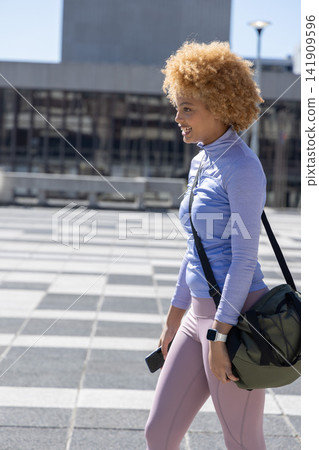 African American woman walking tiled plaza wearing zip top leggings duffel phone watch, copy space African American woman walking tiled plaza wearing zip top leggings duffel phone watch, copy space 141909596