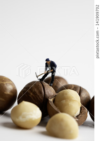 A miniature man cracking macadamia shells with a pickaxe A miniature man cracking macadamia shells with a pickaxe 141909702