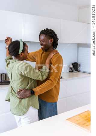 African American female partners hugging and smiling in modern white kitchen near cutting board African American female partners hugging and smiling in modern white kitchen near cutting board 141910232