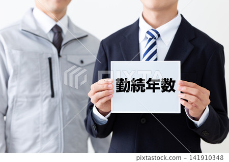 A young businessman in a business suit holding a whiteboard displaying years of service. A young businessman in a business suit holding a whiteboard displaying years of service. 141910348