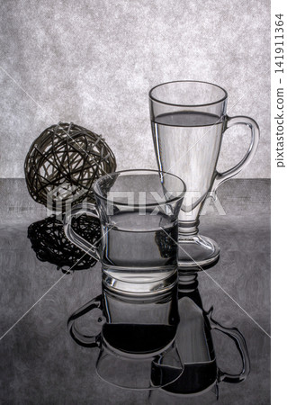 Still life with glass goblets and an abstract object on a gray background Still life with glass goblets and an abstract object on a gray background 141911364