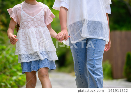 Sisters walking hand in hand along a summer greenway Sisters walking hand in hand along a summer greenway 141911822