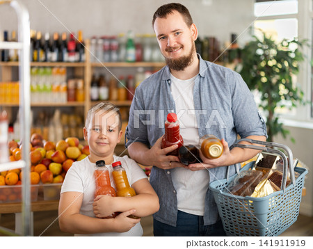Preteen boy with father choosing juices in bottles in supermarket Preteen boy with father choosing juices in bottles in supermarket 141911919