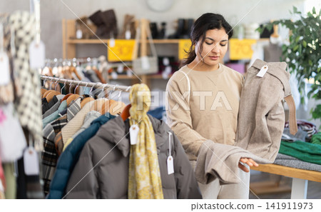 Latin girl is busy looking at clothes items in store, she chooses trousers Latin girl is busy looking at clothes items in store, she chooses trousers 141911973