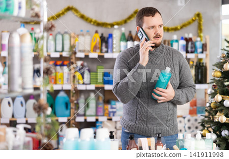 Middle-aged guy speaking on mobile phone while shopping in store during Christmas Middle-aged guy speaking on mobile phone while shopping in store during Christmas 141911998