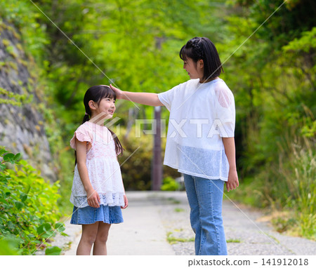 A scene of close sisters outdoors, where the older sister gently strokes the younger sister's head. A scene of close sisters outdoors, where the older sister gently strokes the younger sister's head. 141912018